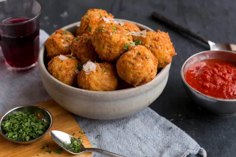 Bowl of golden fried arancini rice balls topped with shaved parmesan and parsley, served with marinara and red wine at Spacca Napoli Pizzeria