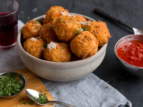 Bowl of golden fried arancini rice balls topped with shaved parmesan and parsley, served with marinara and red wine at Spacca Napoli Pizzeria