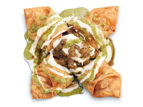 Four crisp samosas arranged around chickpea chaat with green and white chutneys