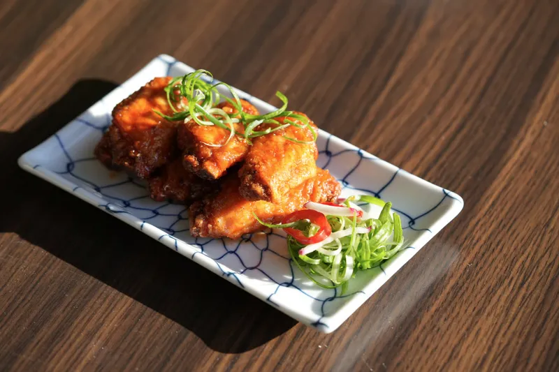 A plate of Dumpling Time's glazed crispy fried chicken topped with scallion curls, on a blue net-patterned plate
