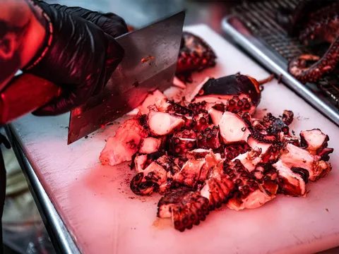 A gloved cook chopping charcoal-grilled octopus (pulpo) on a white cutting board at Evil Cooks in Los Angeles