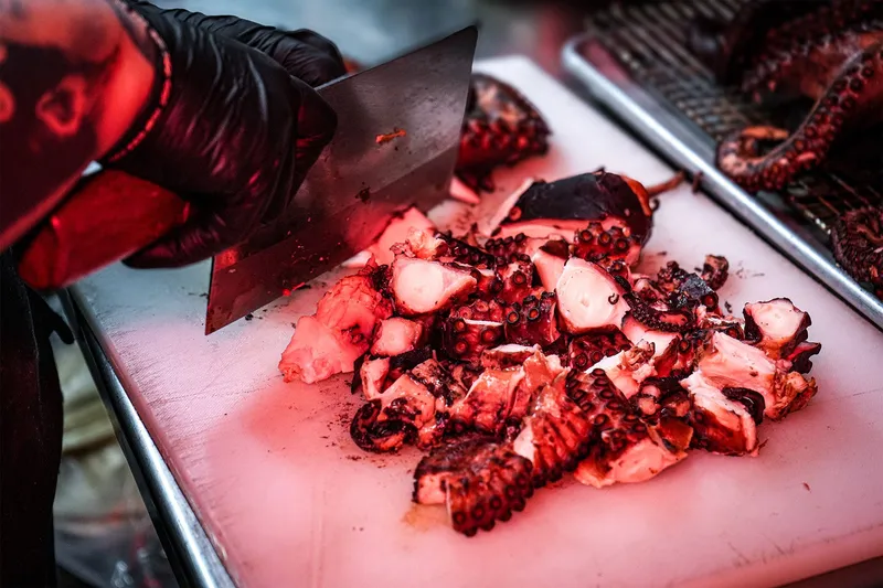 A gloved cook chopping charcoal-grilled octopus (pulpo) on a white cutting board at Evil Cooks in Los Angeles