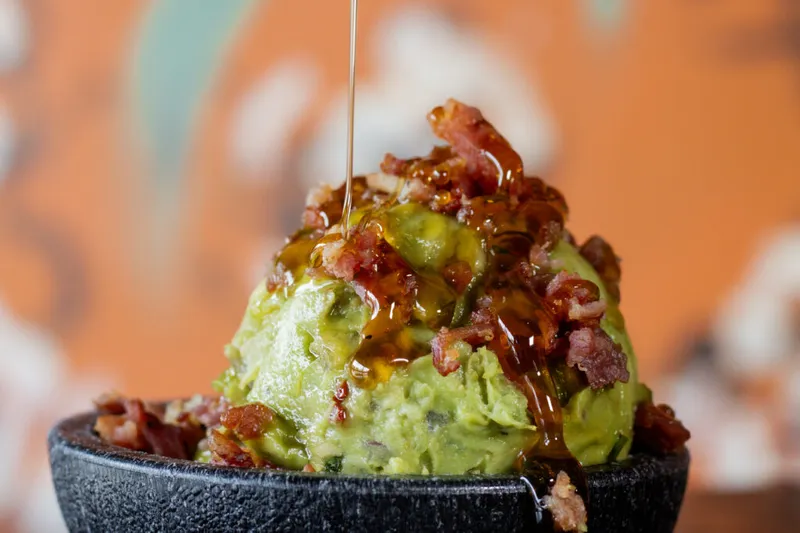 Guacamole in a stone molcajete topped with bacon and drizzled with hot honey at Barrio Tacos