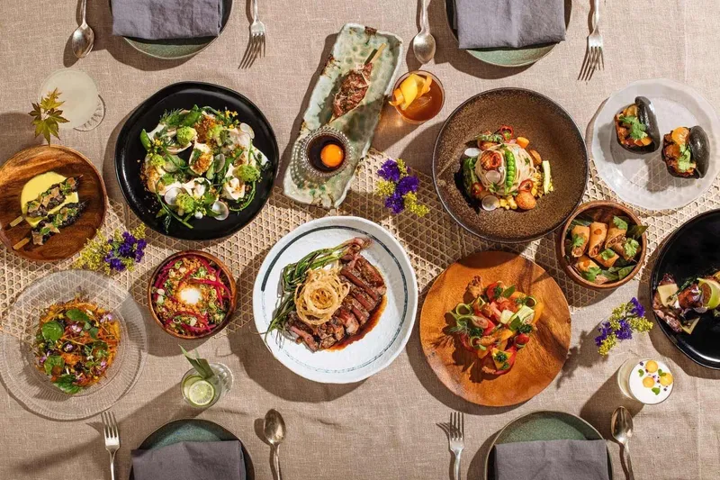 Overhead spread of Filipino dishes at Abacá in San Francisco, including a sliced grilled steak with charred scallions, chilled noodles, a carrot salad, and small plates garnished with edible flowers