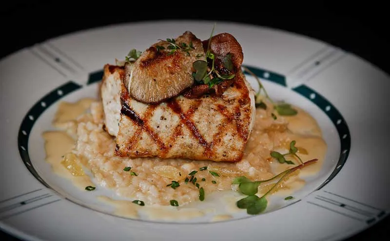 Grilled fish fillet with a seared mushroom served over risotto and microgreens on a plate at Cliff Bell's in Detroit