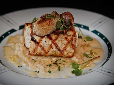 Grilled fish fillet with a seared mushroom served over risotto and microgreens on a plate at Cliff Bell's in Detroit