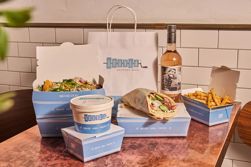 A Souvla takeout spread of a Greek salad, gyro-style pita sandwich, Greek fries, avgolemono soup, and rosé at Souvla in San Francisco.