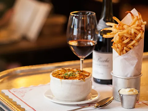 Balthazar's onion soup gratinée with a cone of pommes frites and a glass of red wine on a bistro tray