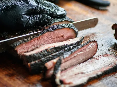 Gloved pitmaster slicing a peppery, bark-crusted smoked brisket on a wooden board at ZZQ Texas Craft Barbeque, Richmond