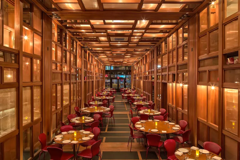 Wood-paneled main dining room at ilili in NoMad, New York, with round tables, red leather chairs, and coffered wood ceiling