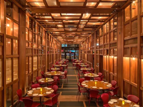 Wood-paneled main dining room at ilili in NoMad, New York, with round tables, red leather chairs, and coffered wood ceiling