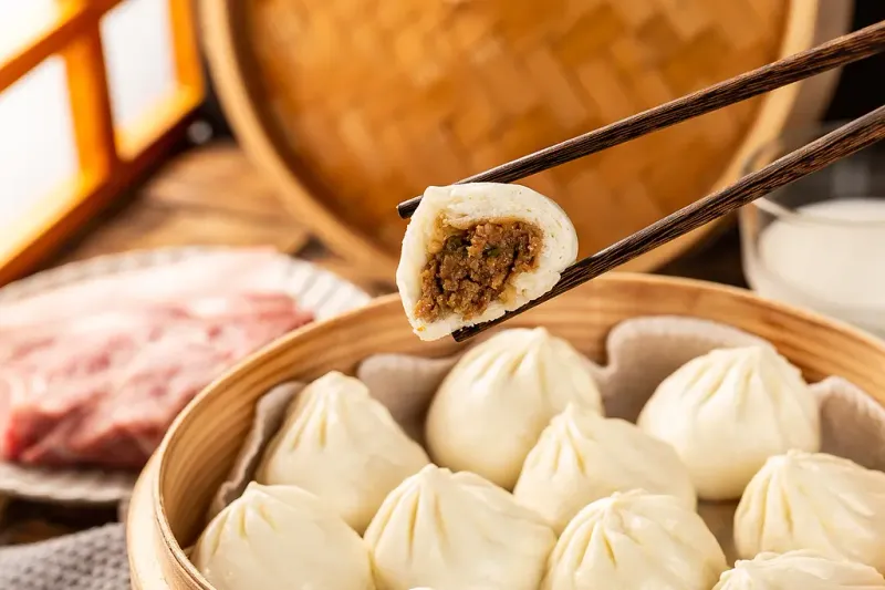 A bitten steamed pork soup dumpling held with chopsticks over a bamboo steamer of soup dumplings at Tom's Dim Sum