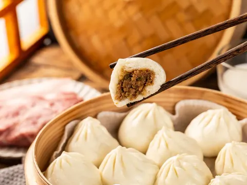 A bitten steamed pork soup dumpling held with chopsticks over a bamboo steamer of soup dumplings at Tom's Dim Sum