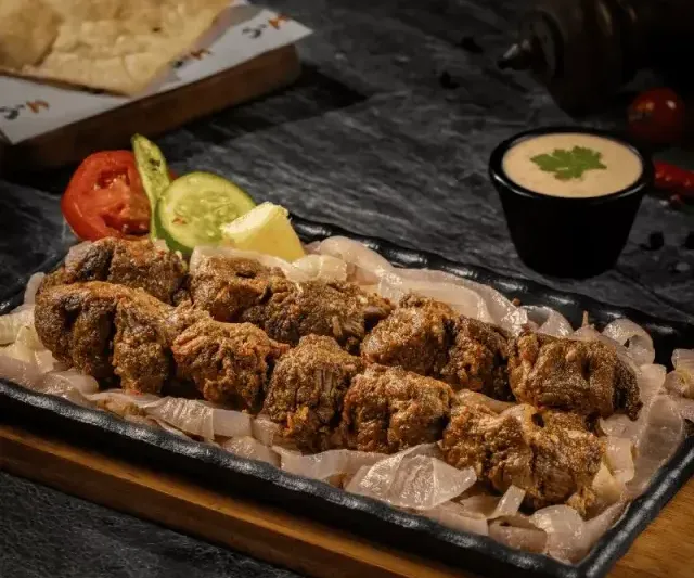 Grilled beef boti skewers served over onions on a sizzling platter with naan at Kababjees.