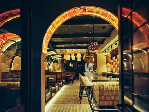 Arched, warmly lit dining room at Adda, with tables along a tiled floor and a bar at the far end
