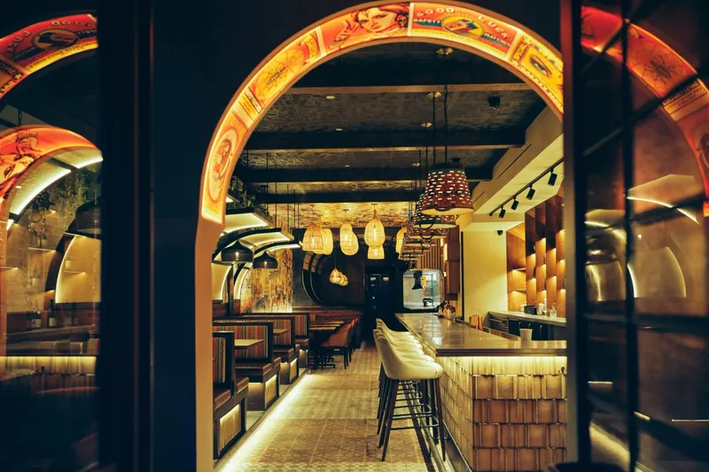 Arched, warmly lit dining room at Adda, with tables along a tiled floor and a bar at the far end