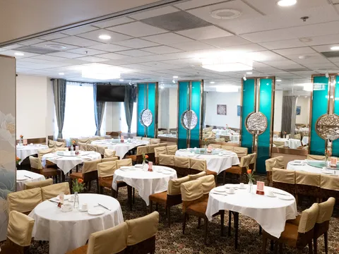 Interior banquet dining room at Peony Seafood Restaurant in Oakland, with round tables set with white linens, lazy Susans, and teal-and-gold decorative screens