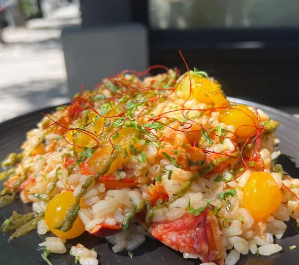 Lobster risotto with cherry tomatoes and herbs on a dark plate outside Mill's Tavern in Providence