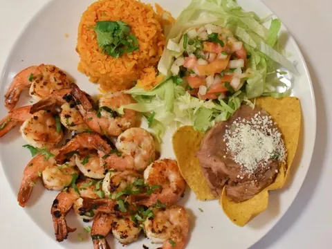 A grilled shrimp plate at El Taco Riendo with Mexican rice, a green salad with pico de gallo, and refried beans topped with cotija on a tostada