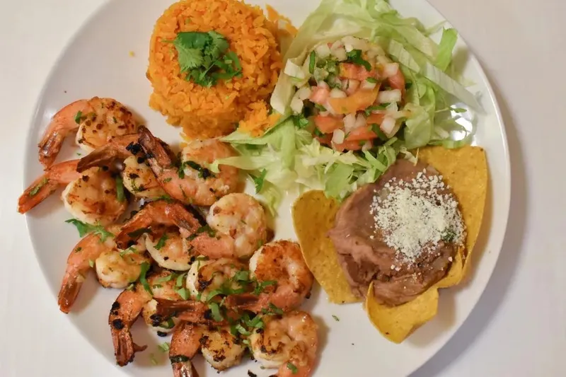 A grilled shrimp plate at El Taco Riendo with Mexican rice, a green salad with pico de gallo, and refried beans topped with cotija on a tostada