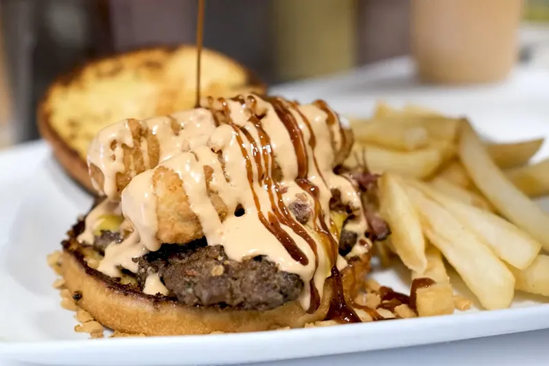 Burger topped with fried onions and sauce, served with fries, at Finger Foods
