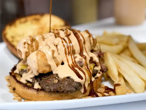 Burger topped with fried onions and sauce, served with fries, at Finger Foods