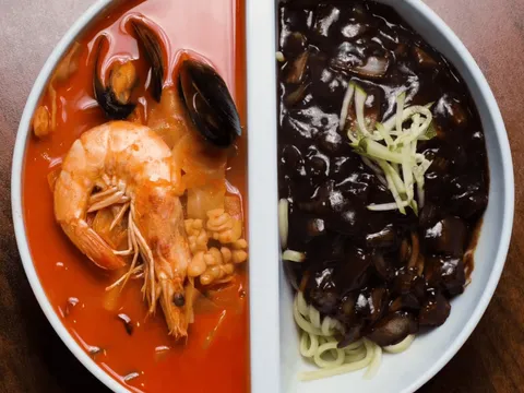 Split bowl of jjamppong spicy seafood noodle soup with shrimp and mussels beside black-bean jjajangmyeon noodles at Man Chun Hong
