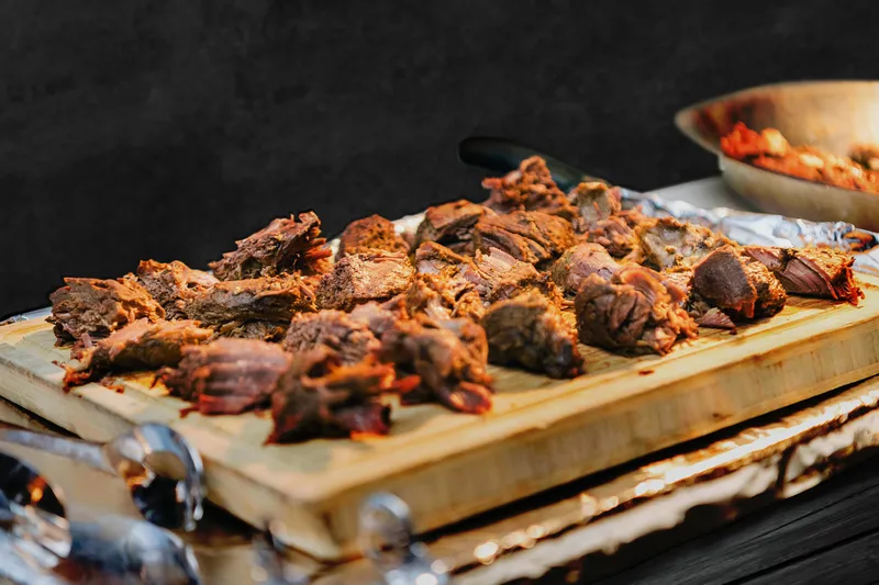 Wooden board of charcoal-barbecued meat from Anmol's catering spread