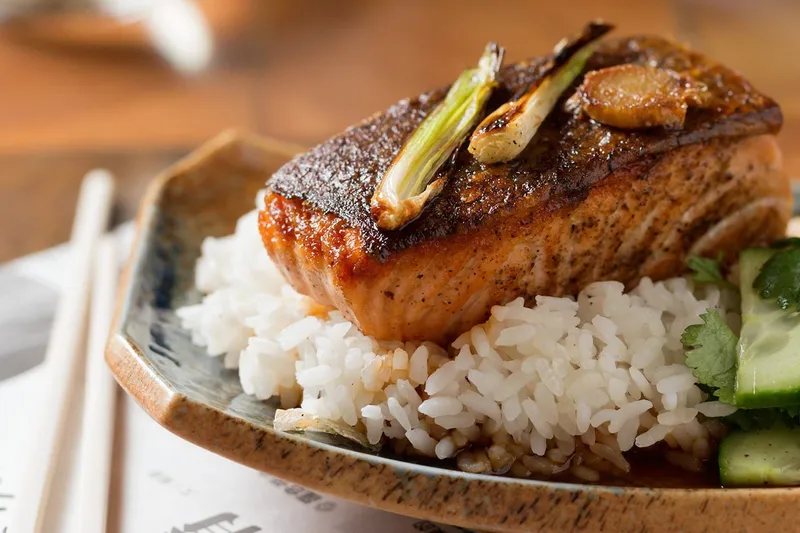 Crispy-skinned soy-glazed salmon fillet over white rice with charred scallions, cucumber and cilantro on a ceramic plate at Myers + Chang in Boston