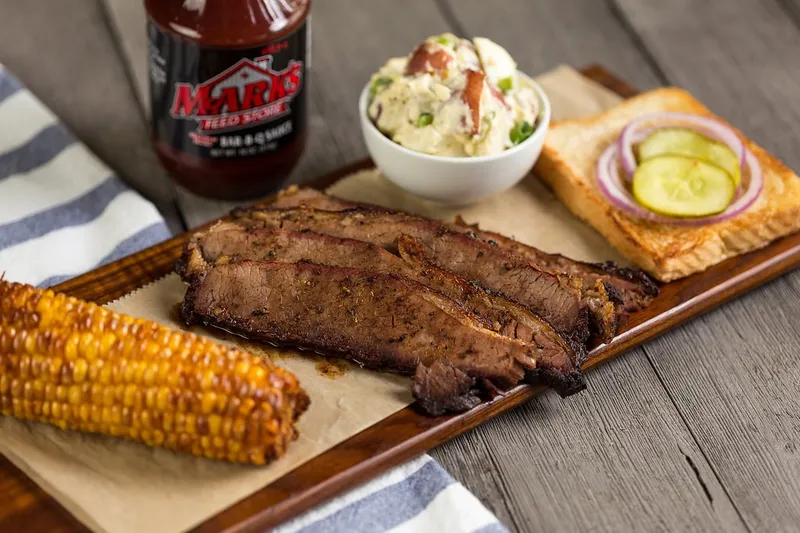 Sliced brisket platter with corn, potato salad and a bottle of Mark's Feed Store barbecue sauce