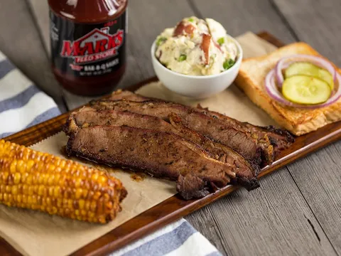 Sliced brisket platter with corn, potato salad and a bottle of Mark's Feed Store barbecue sauce