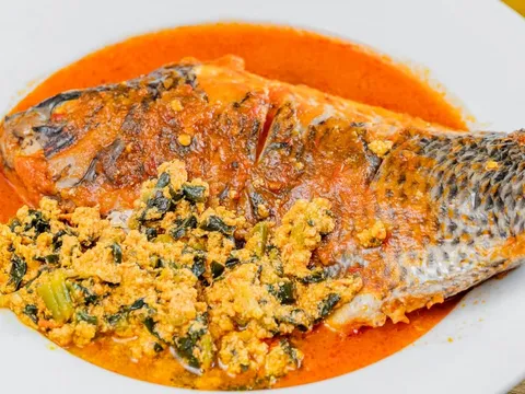 Whole fish simmered in red pepper sauce with egusi (ground melon seed and greens) on a white plate at Buka, Brooklyn