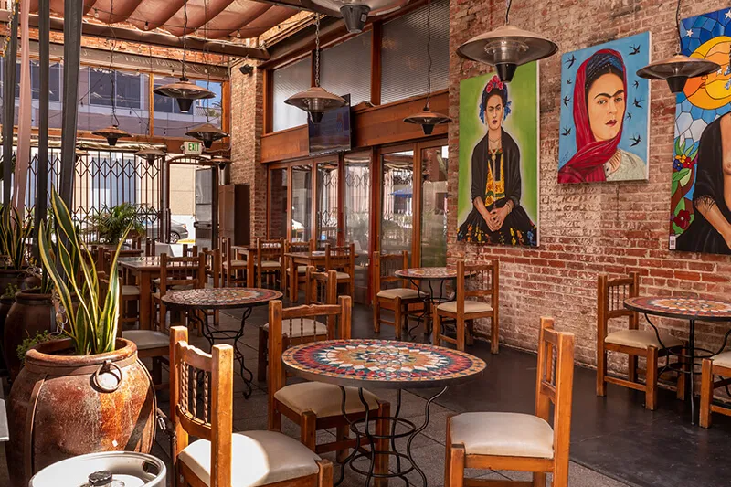 Mezcal's brick-walled dining room in downtown San Jose with mosaic-tile bistro tables, wooden chairs and painted portraits on the wall
