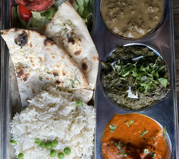 A thali platter at Mela in Boston with tandoori chicken and salad, dal, spinach curry, a red-hued curry, basmati rice with peas, and naan