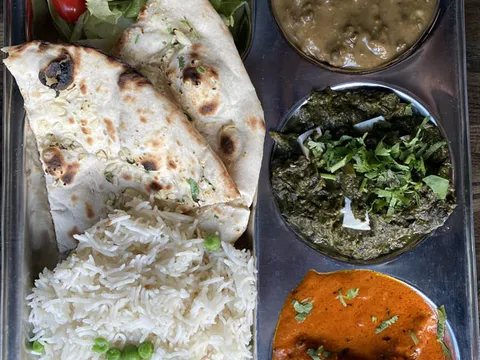 A thali platter at Mela in Boston with tandoori chicken and salad, dal, spinach curry, a red-hued curry, basmati rice with peas, and naan