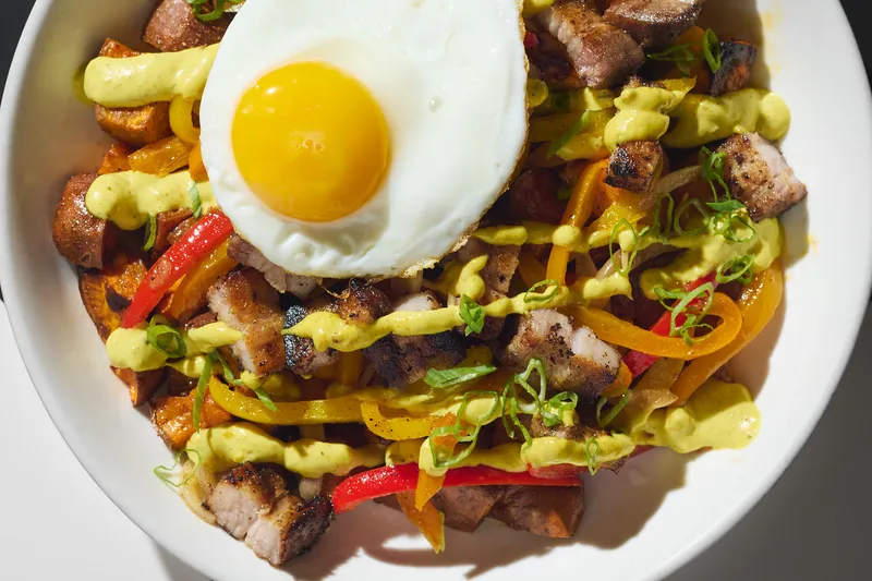 Caribbean rice-and-pepper bowl with roast pork belly, peppers, scallions and a fried egg, drizzled with green sauce, at Miss Lily's 7A, New York