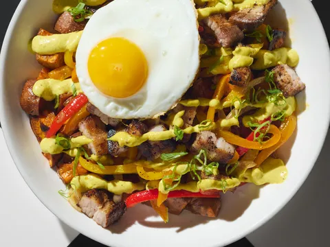 Caribbean rice-and-pepper bowl with roast pork belly, peppers, scallions and a fried egg, drizzled with green sauce, at Miss Lily's 7A, New York