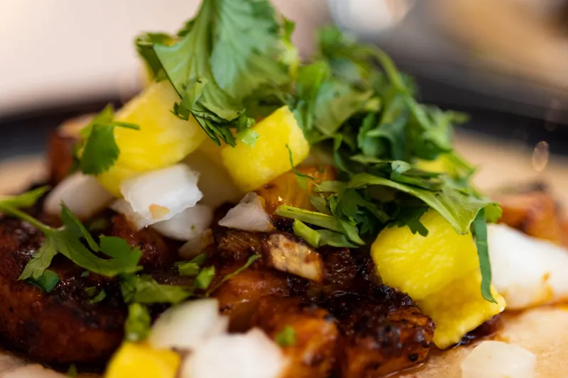 A Taco Luchador al pastor taco on a corn tortilla topped with grilled pineapple, white onion and cilantro