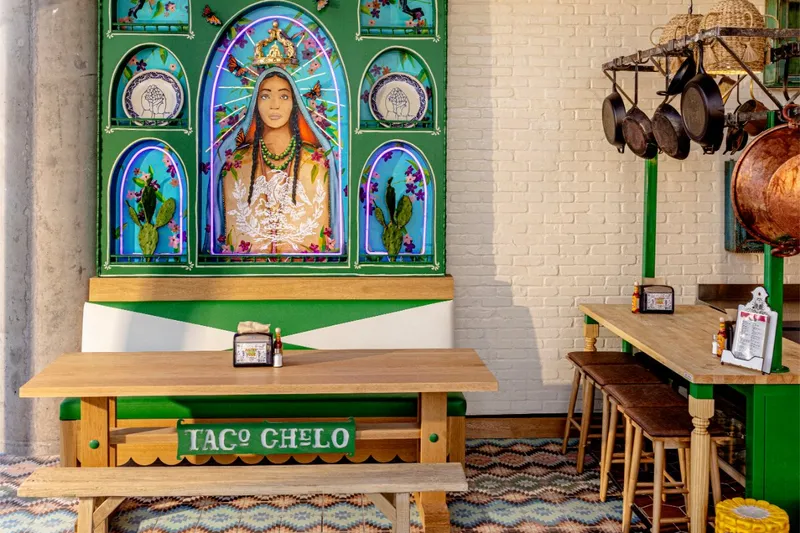 Taco Chelo dining room with a hand-painted Virgen mural, wooden benches, and patterned tile floor