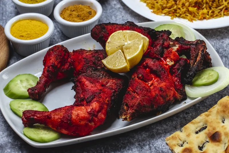 A platter of tandoori chicken at Incredible India in Indianapolis, garnished with lemon and cucumber, served with dishes of spice powders, biryani and naan