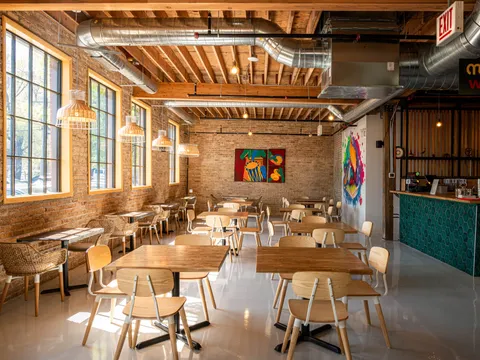 Dining room at Thattu, with exposed brick, wooden tables and daylight from tall windows