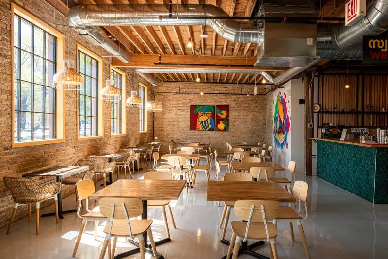 Dining room at Thattu, with exposed brick, wooden tables and daylight from tall windows