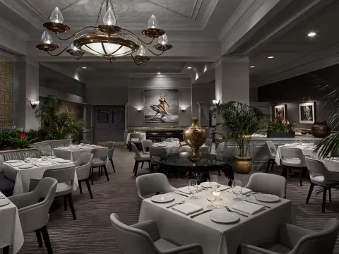 The Bombay Club dining room in Washington, DC, with white-clothed tables, gray armchairs, a brass chandelier, and a brass samovar centerpiece