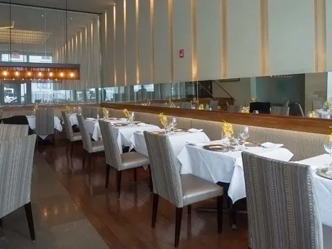 The elegant white-tablecloth main dining room at Tamarind Tribeca in New York, with set tables, patterned banquette seating and a mirrored wall