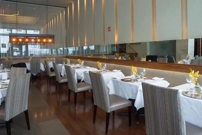 The elegant white-tablecloth main dining room at Tamarind Tribeca in New York, with set tables, patterned banquette seating and a mirrored wall