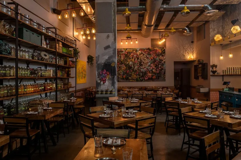 Warmly lit Ghee Indian Kitchen dining room with wooden tables and a colorful spice display