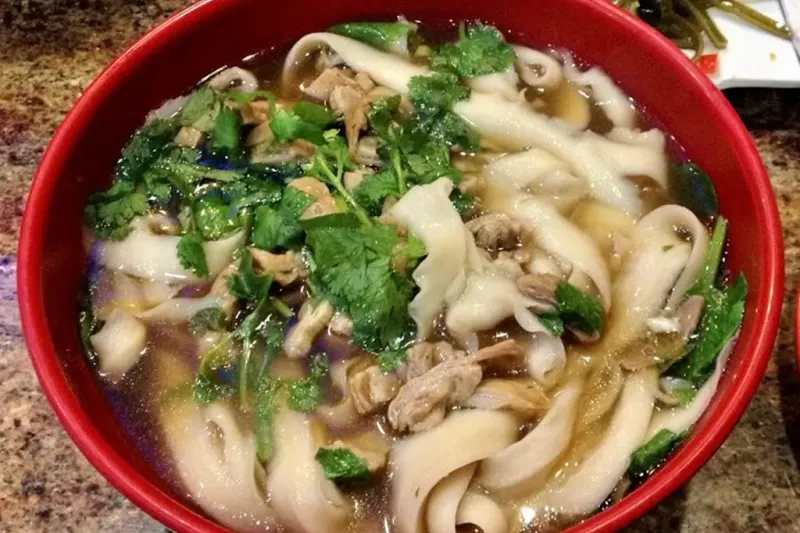 Bowl of hand-drawn wide noodle soup with sliced meat and fresh cilantro at Nan Zhou Hand Drawn Noodle House in Philadelphia