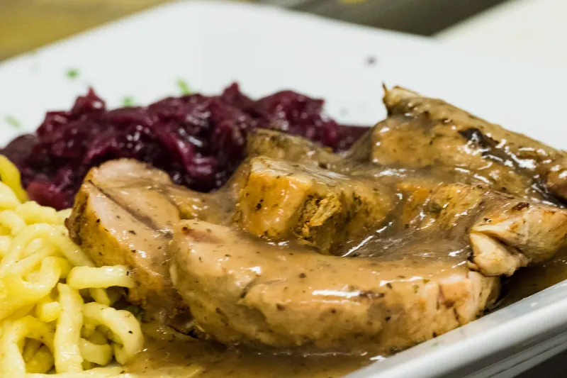 Plate of sliced German pork roast with brown gravy, buttered spaetzle, and red cabbage at Edelweiss German Restaurant in Colorado Springs
