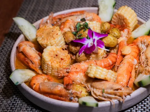 A seafood botana at Picanta Mexican Kitchen — head-on shrimp, corn cobettes, baby potatoes and cucumber in a spiced orange broth, garnished with a purple orchid in a stoneware bowl