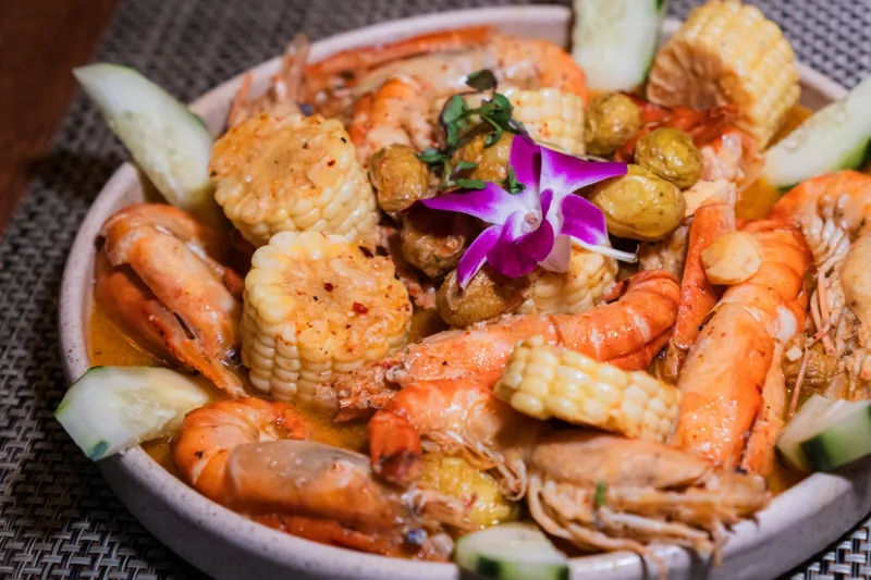 A seafood botana at Picanta Mexican Kitchen — head-on shrimp, corn cobettes, baby potatoes and cucumber in a spiced orange broth, garnished with a purple orchid in a stoneware bowl
